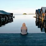 un hombre sentado a la orilla de un lago escandinavo rodeado de casas dentro del agua