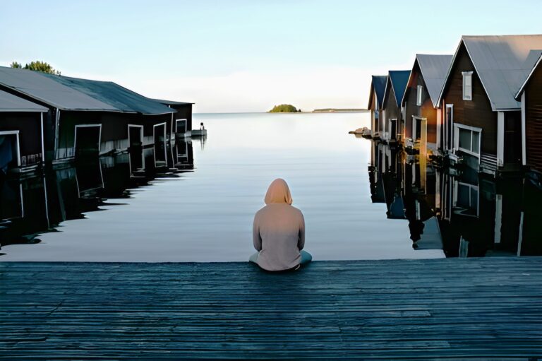 un hombre sentado a la orilla de un lago escandinavo rodeado de casas dentro del agua