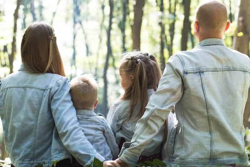 un hombre, una mujer y dos niños sentados en el suelo de un bosque mirando los arboles del fondo