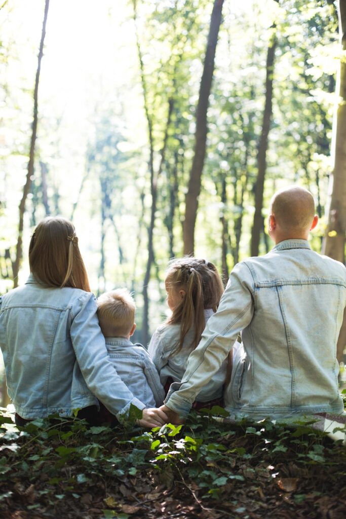 un hombre, una mujer y dos niños sentados en el suelo de un bosque mirando los arboles del fondo